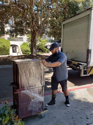 A mover steadying wrapped furniture on a dolly beside a moving truck